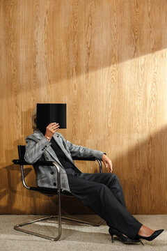Person sitting in chair with notebook covering face