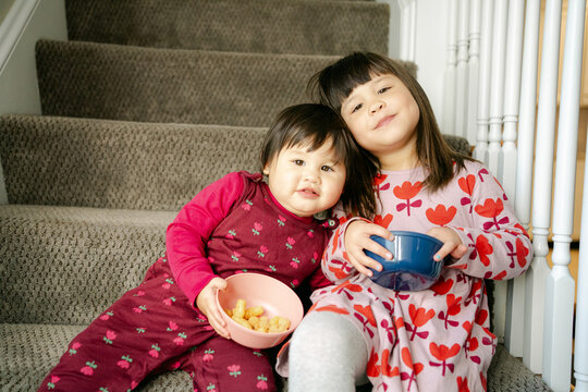 two little girls, sisters, eating snacks on the stairs 