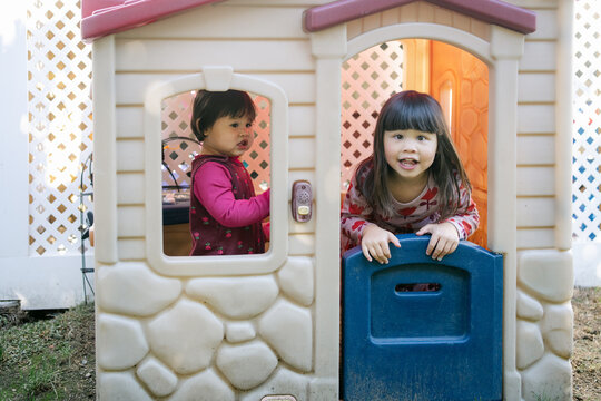 happy sisters playing in playhouse in yard 