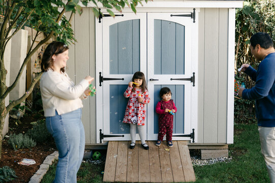 happy family of four in their yard, blowing bubbles 