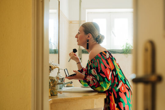 Woman applying makeup with brush at bathroom sink