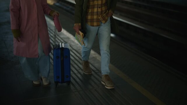 Tourists walk along a city platform with a suitcase and a map. The couple explores an urban environment, ready for adventure.