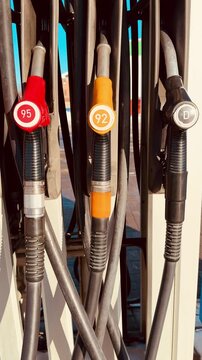 Closeup gas pump nozzles red yellow, octane labels and diesel marker, metal handles and rubber hoses, sunlight highlights textured.