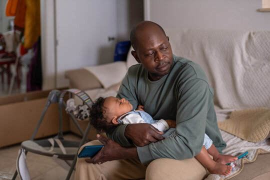 Father Holds Sleeping Baby in Living Room While Sitting on Couch