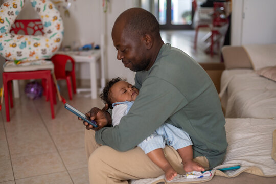 Smiling Father Holds Baby While Using Phone in Living Room
