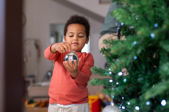 Child Decorating Christmas Tree With Silver Ornament in Home