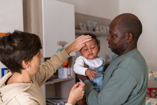 Mother checking baby's forehead for fever while father holds him