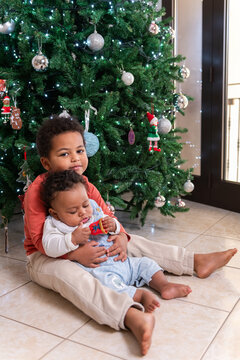 Two siblings sitting near Christmas Tree During Holiday Season