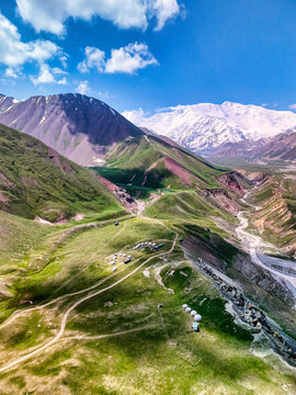 Aerial view of a traditional yurt camp near Tulpar Lake on green mountain slopes with snow-capped peaks in the background Alay District, Osh Region, Kyrgyzstan.