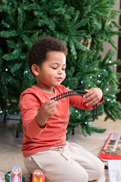 A Curious Child Interacts With Toy Train Tracks Near Christmas Tree