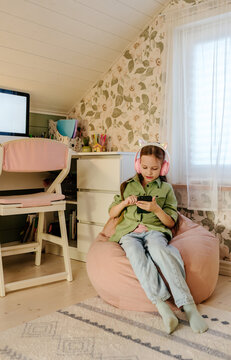 Child Using Smartphone with Headphones in Cozy Home Study Room