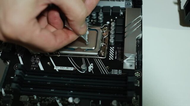Hands applying thermal paste to a motherboard processor with tweezers. Close-up of a PC assembly.