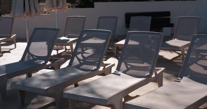 PORTOCOLOM, MALLORCA, SPAIN - OCTOBER, 2025: Midday sun illuminates empty sun loungers, harsh light and long shadows create strong contrast and cool atmosphere