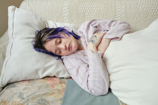 Tattooed person looking introspective lying down in the couch