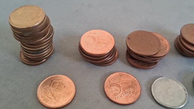 Multiple stacks of Brazilian coins organized on a flat grey surface captured in motion video footage
