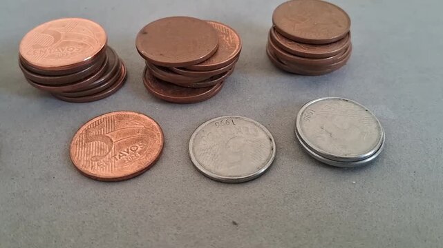 Brazilian coins arranged in small stacks across a flat gray surface in this motion video footage