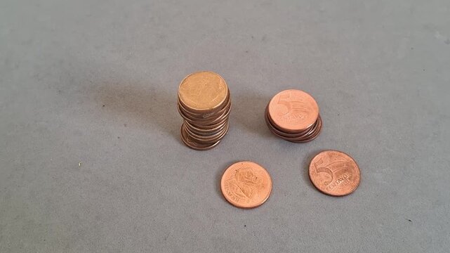 Brazilian five centavos coins stacked and arranged on a grey surface by a moving hand, close-up video.