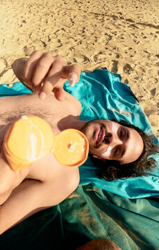Person applying sunscreen while relaxing on sandy beach