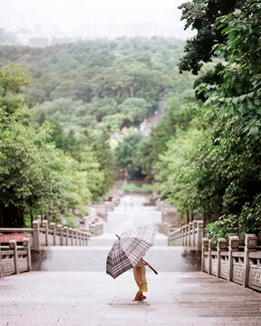 A little girl with an umbrella walks up a long park staircase