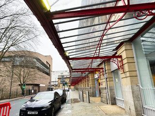 Obraz premium Red glass Manchester Victoria Station canopy over a wet Manchester, UK street with historic stone facades, ornate ironwork and parked cars creating an urban rainy day perspective