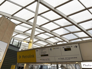 Obraz premium Metrolink station interior with modern glass canopy and directional signage at Manchester UK tram stop showing platforms tickets toilets and way out