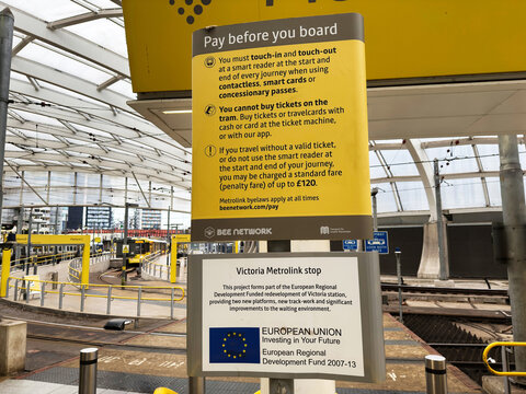 Victoria Metrolink stop in Manchester, UK with pay before you board sign and passengers at city tram station