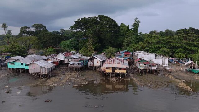 Backward aerial pull above a coastal village of stilt homes exposed at low tide with muddy foreshore and bangka outriggers in Puerto Princesa on the island of Palawan Philippines