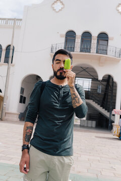 Young man with tattoos covering his eye with an ice pop.