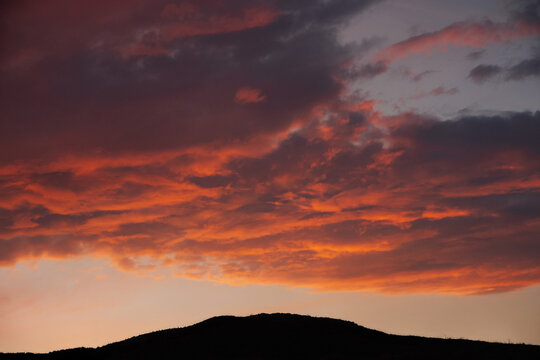Sunset with orange clouds over a hill silhouette