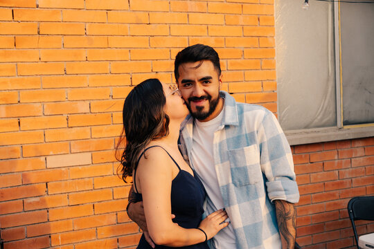 Young couple laughing and embracing in front of a brick wall.