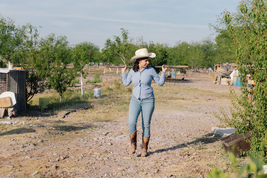 Cowgirl walking with tools on her shoulders in a field.