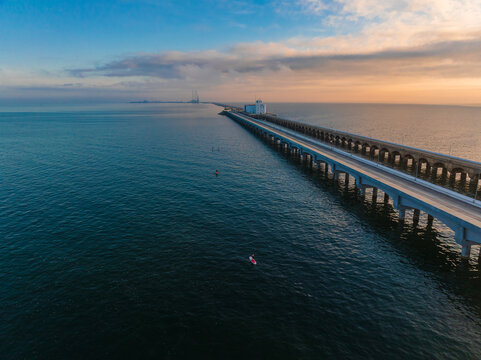 Aerial view of the long Progreso Pier stretching across the calm blue ocean with people on paddleboards under a soft sunset sky in Yucatan, Mexico.