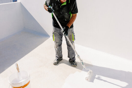 Unidentified elderly painter rolling white paint onto a terrace floor