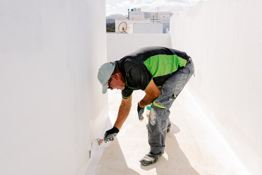 Painter bending down to apply paint to the lower section of a wall