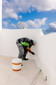 A painter, leaning over to paint the bottom part of a wall
