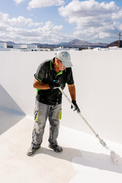 Painter spreading white paint across a terrace floor with a roller