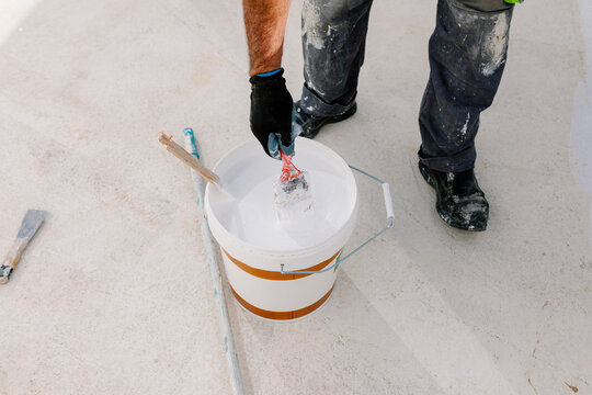 Anonymous painter's hand dipping a brush into a pot of white paint