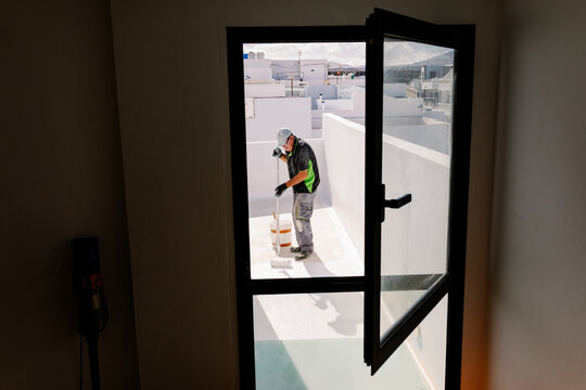 Elderly man painting a terrace, seen from inside a window