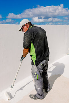 Elderly painter using a roller to coat the floor of a white terrace