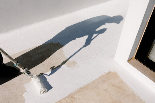 Shadow of unknown man cast on ground as he uses a roller to paint