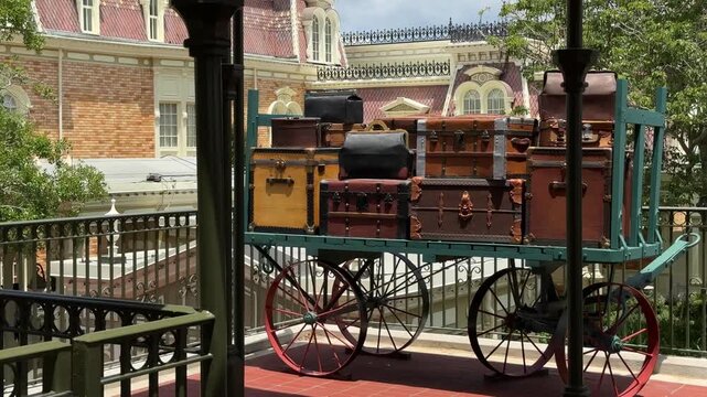 A display of vintage suitcases sits on a railway station platform near historic buildings. The scene represents classic travel, luggage, and transportation history.