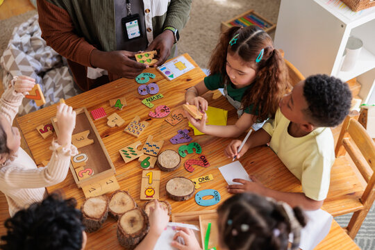 Teacher and children learn numbers with wooden puzzles and blocks.