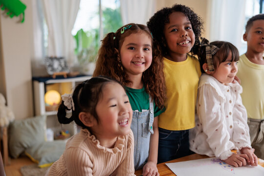 Smiling children of diverse backgrounds stand together indoors.