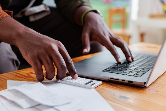 Man calculates bills on laptop with calculator.