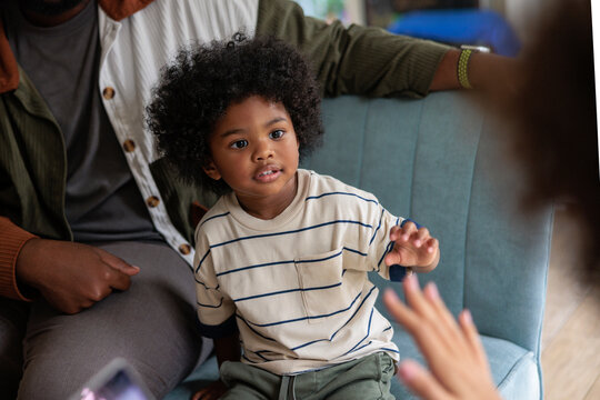 Young boy sits with family, reaching out with hand.