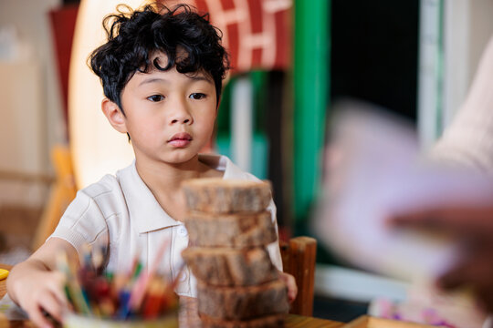 Young boy stacks wood slices, focused on the task.