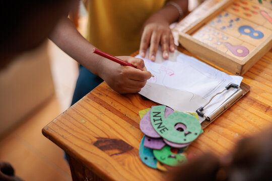 Child draws on paper with number learning tools nearby.