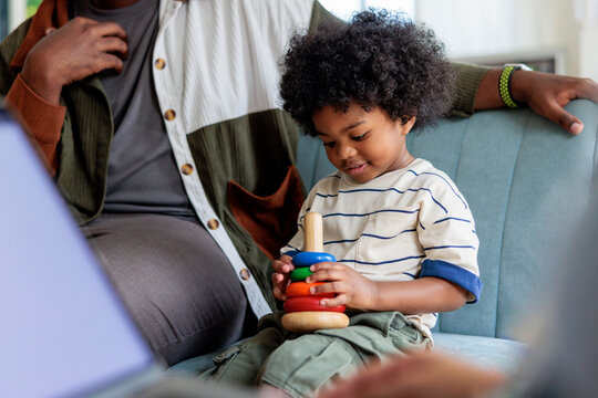 Child plays with stacking toy, parent nearby.