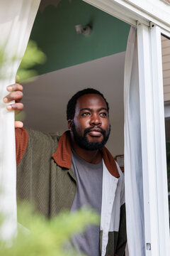 Man looks out window with thoughtful expression.