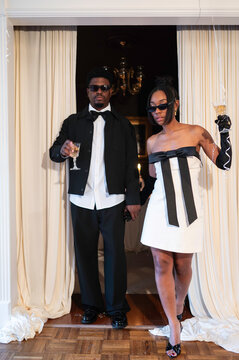 Couple Enters a Party Holding Drinks and Wearing Stylish Outfits